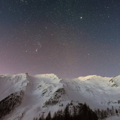 A Breathtaking View Of Snow Capped Mountains Under A Starry Night Sky, Capturing The Beauty Of Winter Outdoors.