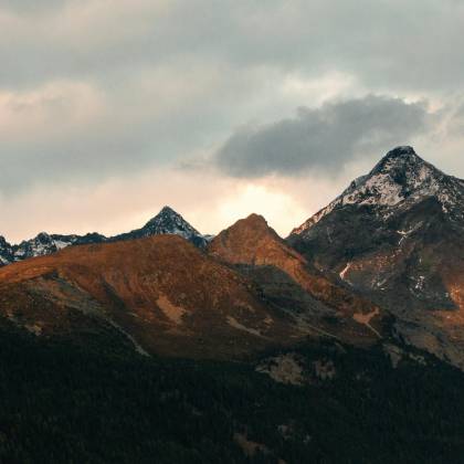 Breathtaking View Of Mountain Peaks Adorned With Snow Under A Cloudy Sky At Dusk.
