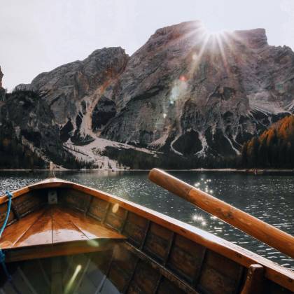 Wooden Boat Sailing On A Serene Mountain Lake With Sunrays Illuminating The Scenic Landscape.