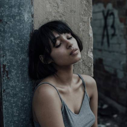 A Young Woman Sits With Eyes Closed In A Quiet Urban Alley, Wearing A Gray Tank Top.