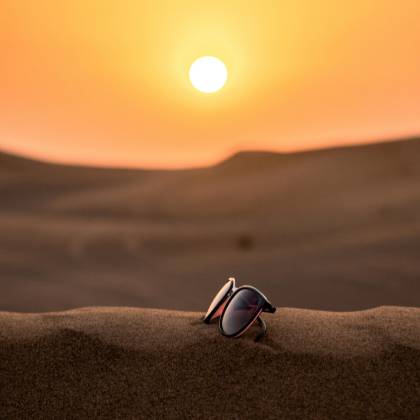 Scenic View Of Sunglasses On Dubai's Desert Sand With A Stunning Sunset Backdrop.
