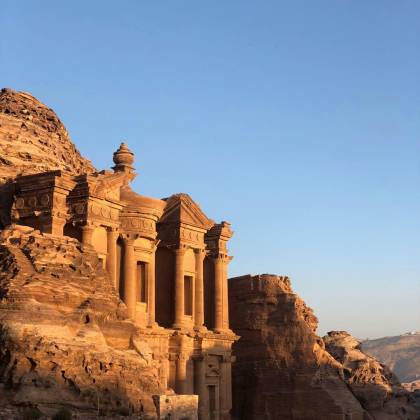 Capture Of The Ancient Petra Monastery In Jordan Illuminated By Sunset, Showcasing Stunning Sandstone Architecture.