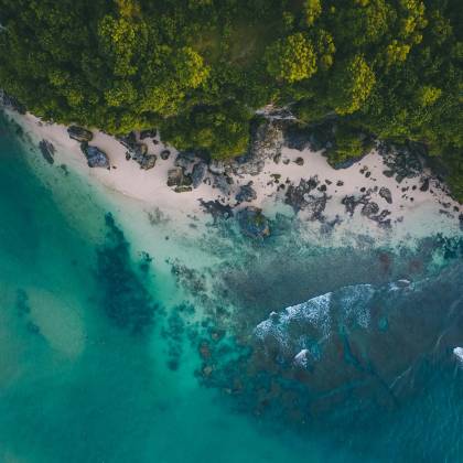 Stunning Aerial View Of A Pristine Beach In Bali With Turquoise Waters And Lush Greenery.